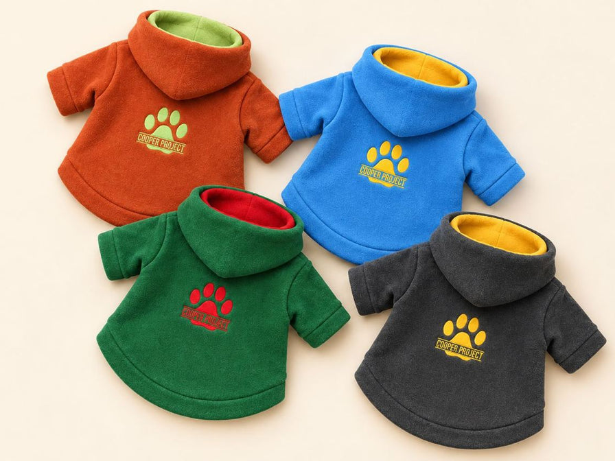 Four Cooper Project dog fleece hoodies laid flat: rust, blue, green and charcoal, each with a contrasting hood lining and the embroidered paw